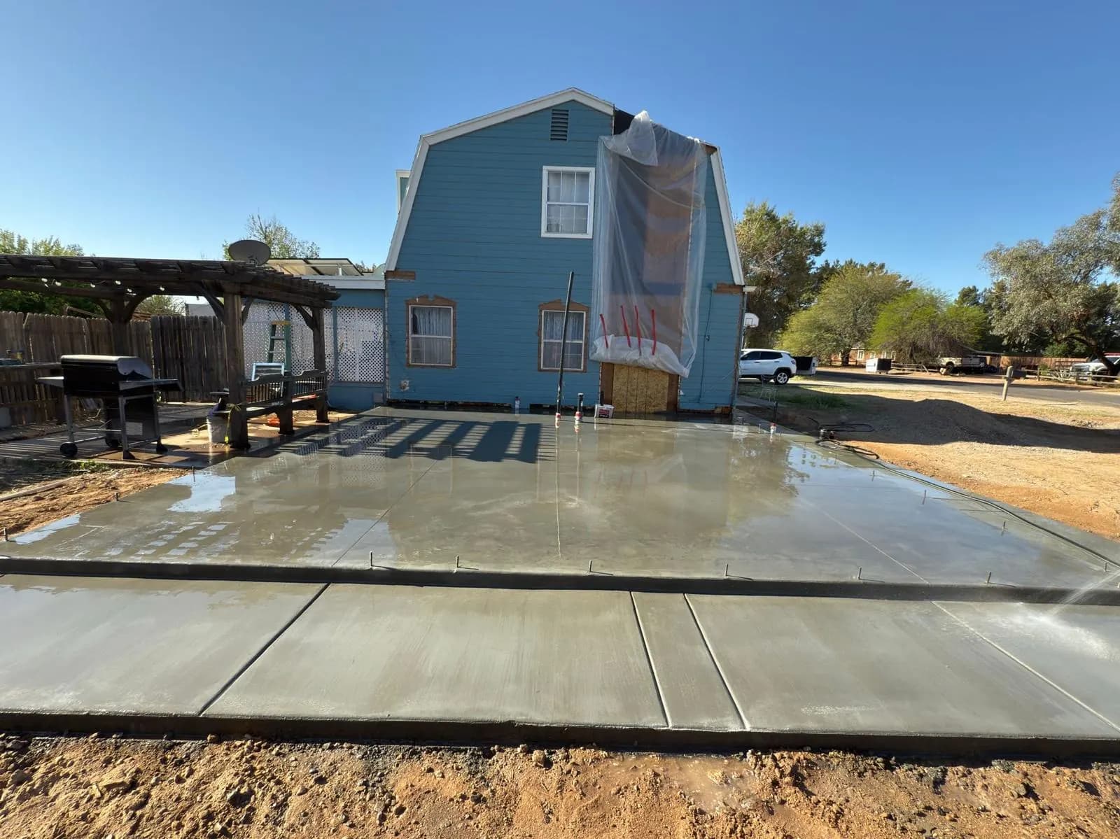 Freshly poured backyard concrete patio slab beside a two-story home with a pergola