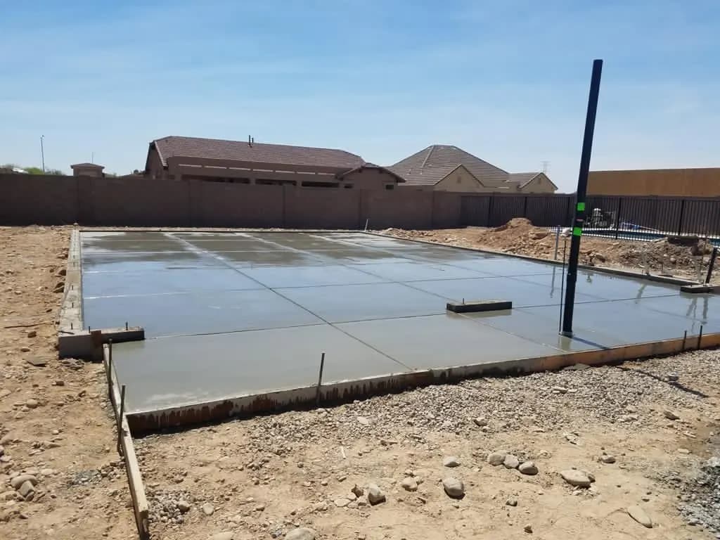Large freshly poured concrete slab in a backyard enclosed by a block wall