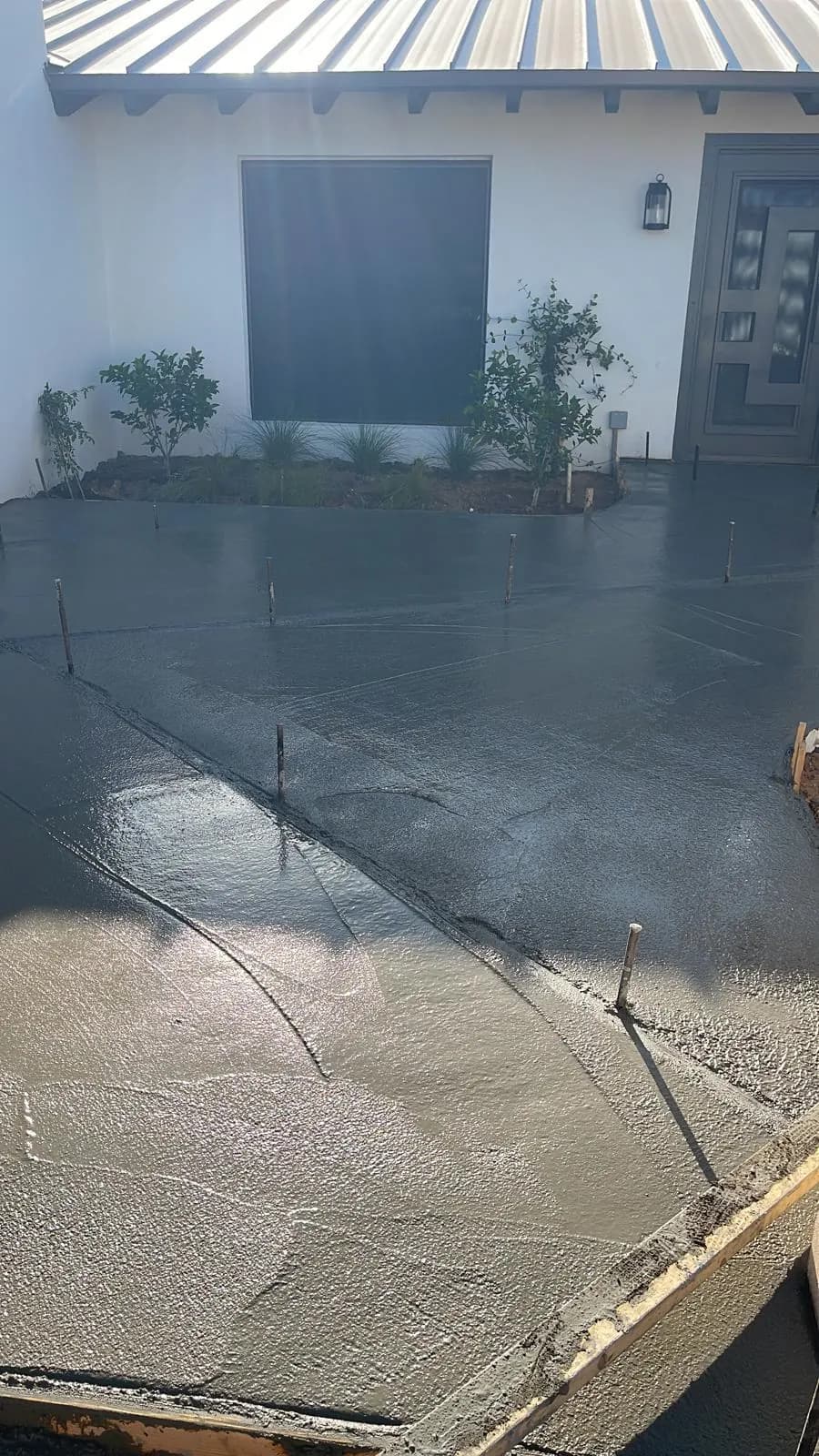 Freshly poured concrete patio slab in front of a white home with a standing-seam metal awning