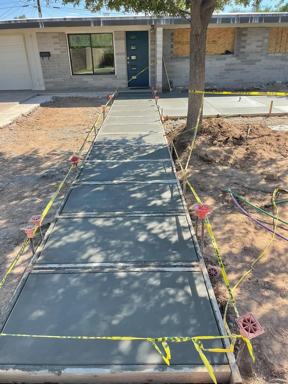 Long freshly poured concrete walkway with control joints, roped off in front of a brick home