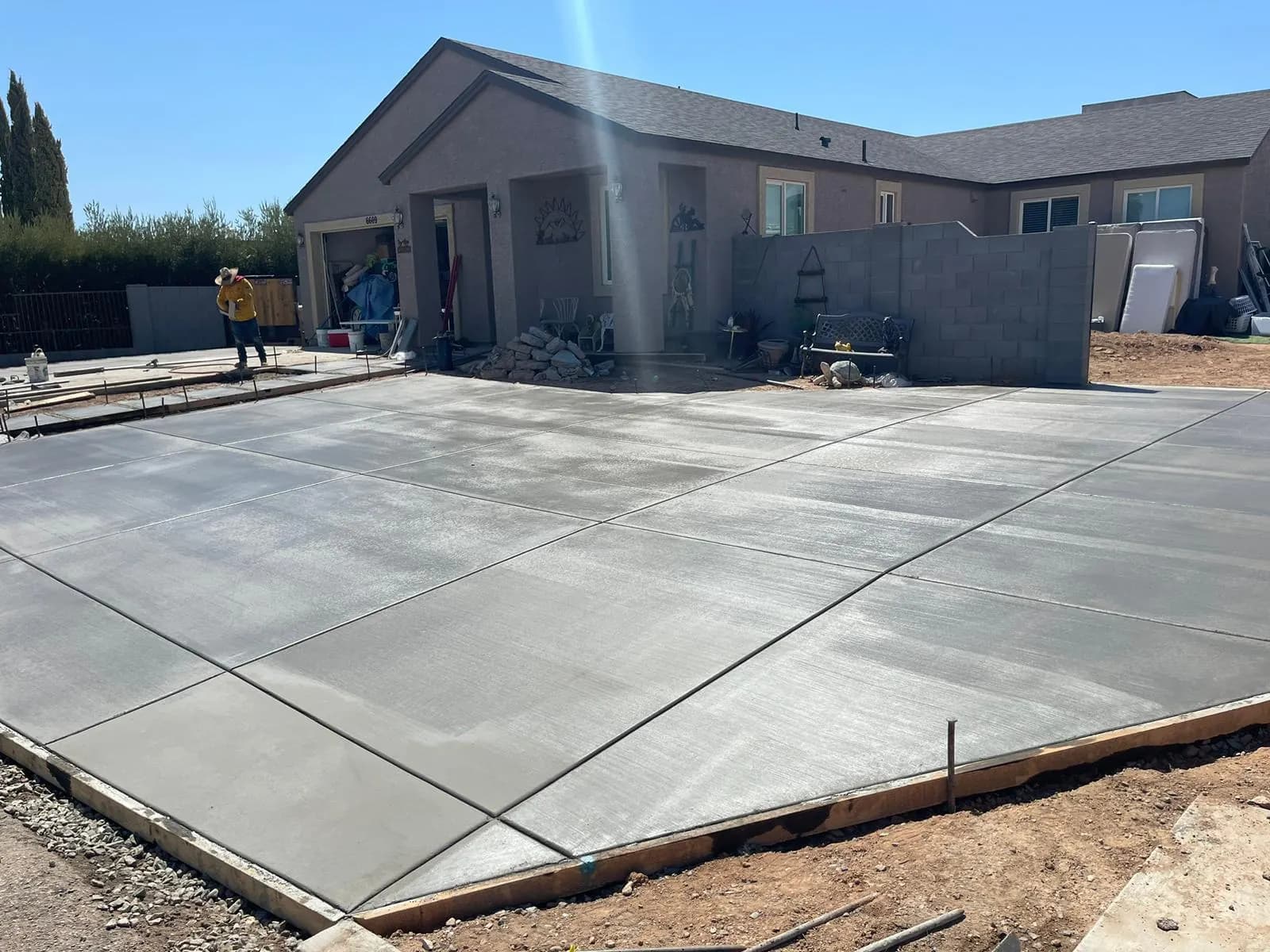 Large finished concrete slab filling a backyard behind a single-story home, with edge forms still in place